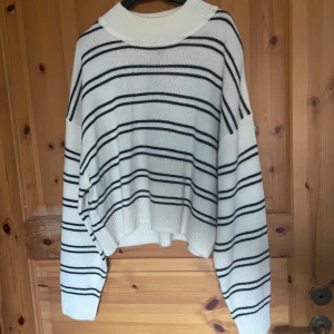 Vit och svart randig stickad tröja - Mysig vit stickad tröja med svarta ränder. Tröjan har en lös passform och långa ärmar, perfekt för kyliga dagar. Den har en rund halsringning och är både stilren och bekväm.