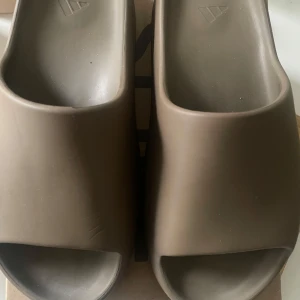Adidas Yeezy Slide Earbrn Storlek 46 - Adidas Yeezy Slide i färgen "Earbrn" i använt skick. Lite märken här o där, se bilder för egen uppskattning. Säljs med originalkartong
