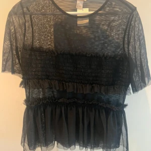 Svart transparent topp med volanger - En superfin svart topp från H&M i storlek S, helt ny. Den har korta ärmar och är dekorerad med volanger. Perfekt för en utekväll eller fest! 🖤