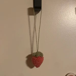Phone charm jordgubbe - En virkad phone charm med en jordgubbe i änden! ☺️ Kan också användas som nyckelring, att hängas på väskan, osv! Fler tillverkas om den säljer! Gjord på 100% bomullsgarn