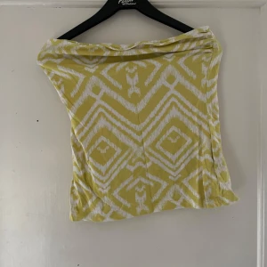Gul och vit mönstrad tubtopp från H&M - Säljer en snygg gul och vit tubtopp från H&M med ett coolt geometriskt mönster. Perfekt för sommardagar eller en festlig kväll. Toppen är i bra skick och superbekväm att bära. Passa på att fynda denna trendiga topp!