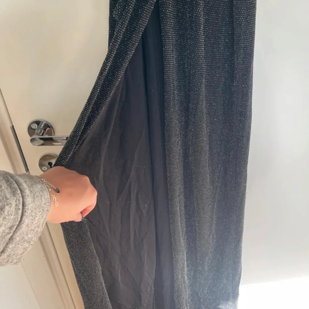 Säljer en elegant svart långklänning med glittriga detaljer. Klänningen har långa ärmar och ett knytband i midjan för en smickrande passform. Perfekt för festliga tillfällen!. Mekot.