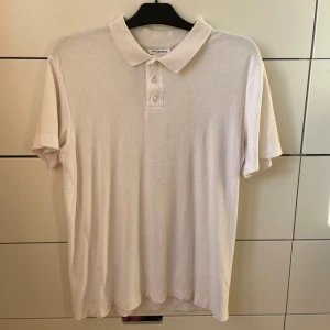 Vit kortärmad pikétröja från Lindbergh - Säljer en stilren vit frottépiké från Lindbergh. Den har en klassisk krage med knappar och är kortärmad, perfekt för både vardag och lite finare tillfällen. Materialet känns mjukt och bekvämt, vilket gör den skön att bära hela dagen.🙂