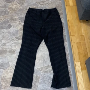 Svarta randiga kostymbyxor - Snygga svarta kostymbyxor med diskreta ränder. Byxorna har en klassisk passform och är perfekta för en stilren look. De är högmidjade och har en rak siluett som ger en elegant touch.