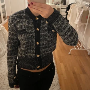 Fin kofta med guldknappar - Snygg svart och vit rutig kofta med glittriga detaljer och guldknappar. Jackan har en croppad passform och långa ärmar. Perfekt för att ge en elegant touch till din outfit.