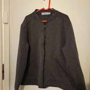 Grå bomberjacka från Sail Racing - Snygg grå bomberjacka från Sail Racing med dragkedja framtill. Tillverkad i en blandning av polyester, viskos och elastan för en bekväm passform. Jackan har ett diskret mönster på ryggen och praktiska fickor.