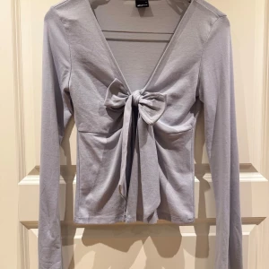 Tie top ifrån Gina tricot  - Snygg ljus lila långärmad topp från Gina Tricot med knytning framtill. Perfekt för en stilren look med en touch av elegans. Toppen har en v-ringad design och är tillverkad i ett mjukt material.