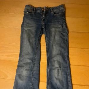 Blå jeans från Lindex  - Snygga blå jeans från Lindex med klassisk femficksdesign och knappgylf. Perfekta för en avslappnad stil. De har en lätt tvättad look som ger en cool vibe. Dem är low waist och bootcut.