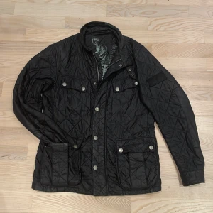 Barbour jacka  - Snygg svart barbour jacka med knappar och dragkedja. Jackan har flera fickor med knappstängning och en stilren design. Skick 9/10 och knappt använd. Perfekt nu till våren. Säljs på grund av att jag inte använder den något mer. Modellen är 181cm och 72kg. Kontakta mig om du är intresserad. priser går att diskutera. Nypris 3000kr