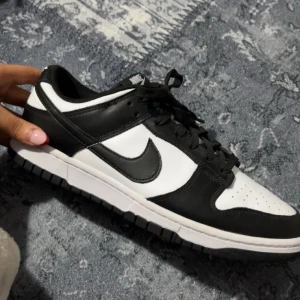 Nike Dunk i svart och vitt - Snygga Nike Dunk sneakers i klassisk svart och vit färgkombination. Skorna har en stilren design med snörning och den ikoniska Nike-loggan på sidan. Perfekta för en sportig och trendig look.