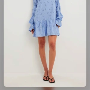 Ljusblå klänning med volang och öppen rygg -  ljusblå klänning från nakd med broderade blommor och volangdetaljer. Den har en öppen rygg med knytband och långa ärmar med resår vid ärmsluten. Använd 2 gånger