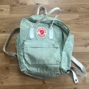 Grön ryggsäck från Fjällräven - Säljer en klassisk grön Fjällräven Kånken ryggsäck med det ikoniska röda logotypmärket på framsidan. Ryggsäcken har justerbara axelremmar och en praktisk dragkedja framtill. Perfekt för vardagsbruk och utflykter.(säljer då den inte kommer till användning längre) köpte för 972kr 
