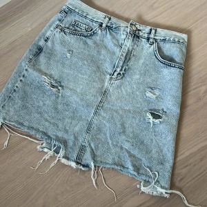 Jeanskjol från LCW - Snygg jeanskjol från LCW i en klassisk blå denimfärg. Kjolen har en rå kant och slitna detaljer för en trendig look. Kjolen är perfekt för sommaren då man kan styla den med en söt topp!