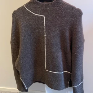 Brun tröja från Zara - Säljer en brun tröja från Zara med en unik vit linjedetalj. Tröjan har en hög krage och långa ärmar, perfekt för kyligare dagar. Den är tillverkad i ett mjukt material som ger en bekväm passform.