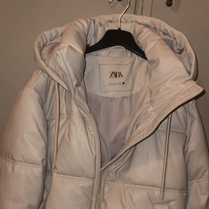 Vit pufferjacka från Zara - Säljer en snygg vit pufferjacka från Zara med dragkedja och huva. Jackan har en quiltad design och långa ärmar, perfekt för kyliga dagar. Storlek S, Använd 1-2 gånger bra skick! 