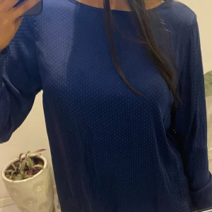 Mörkblå blus med knytning - Snygg mörkblå blus med diskret prickigt mönster. Blusen har långa ärmar och en elegant knytning i ryggen. Perfekt för en stilren look.