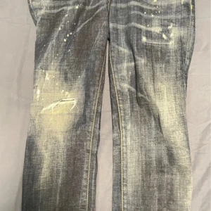 Jeans från DSQUARED2 - Snygga jeans från DSQUARED2 med en cool slitning och färgstänk för en unik look. De har en klassisk femficksdesign och en röd logotyp på bakfickan. Perfekta för dig som vill ha en edgy stil. En sak bara att jag klippte jeansen men den ska vara 3/4 som modellen