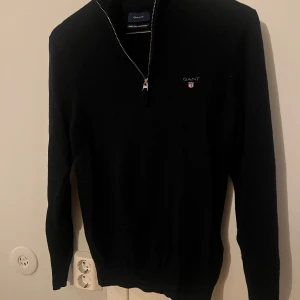 Half zip från GANT - Säljer en stilren svart tröja från GANT i superfin lammull. Tröjan har en dragkedja vid halsen och långa ärmar. Den är lite liten i storleken.                                                     Perfekt för kyligare dagar.