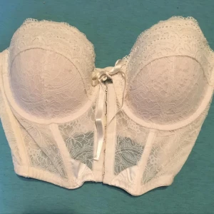 Vit spetskorsett från Bella M 75C - Elegant vit korsett från Bella M i spets med Perfekt för speciella tillfällen med sin romantiska design och detaljerade spetsmönster. Den har en smickrande passform och ger ett stilfullt intryck.Saknas bh banden.. Mycket fint skick! 