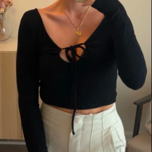Svart croppad topp med knyt - Snygg svart croppad topp med knyt framtill och långa ärmar. Ny skick
