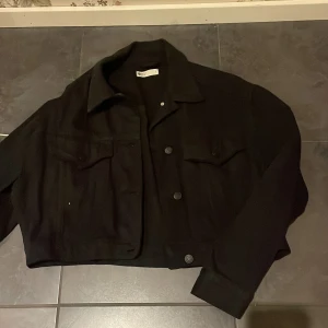 Svart Jeansjacka från Gina Tricot - Snygg svart jeansjacka från Gina Tricot med knappar framtill. Perfekt för en stilren look. Jackan har långa ärmar och två bröstfickor med lock.