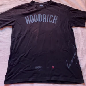 Hoodrich T-shirt  - Snygg svart t-shirt från Hoodrich med tryck på både fram- och baksidan. Perfekt för en casual look. Tillverkad i mjukt material för extra komfort. De är ett litet hål på vänstra armen 