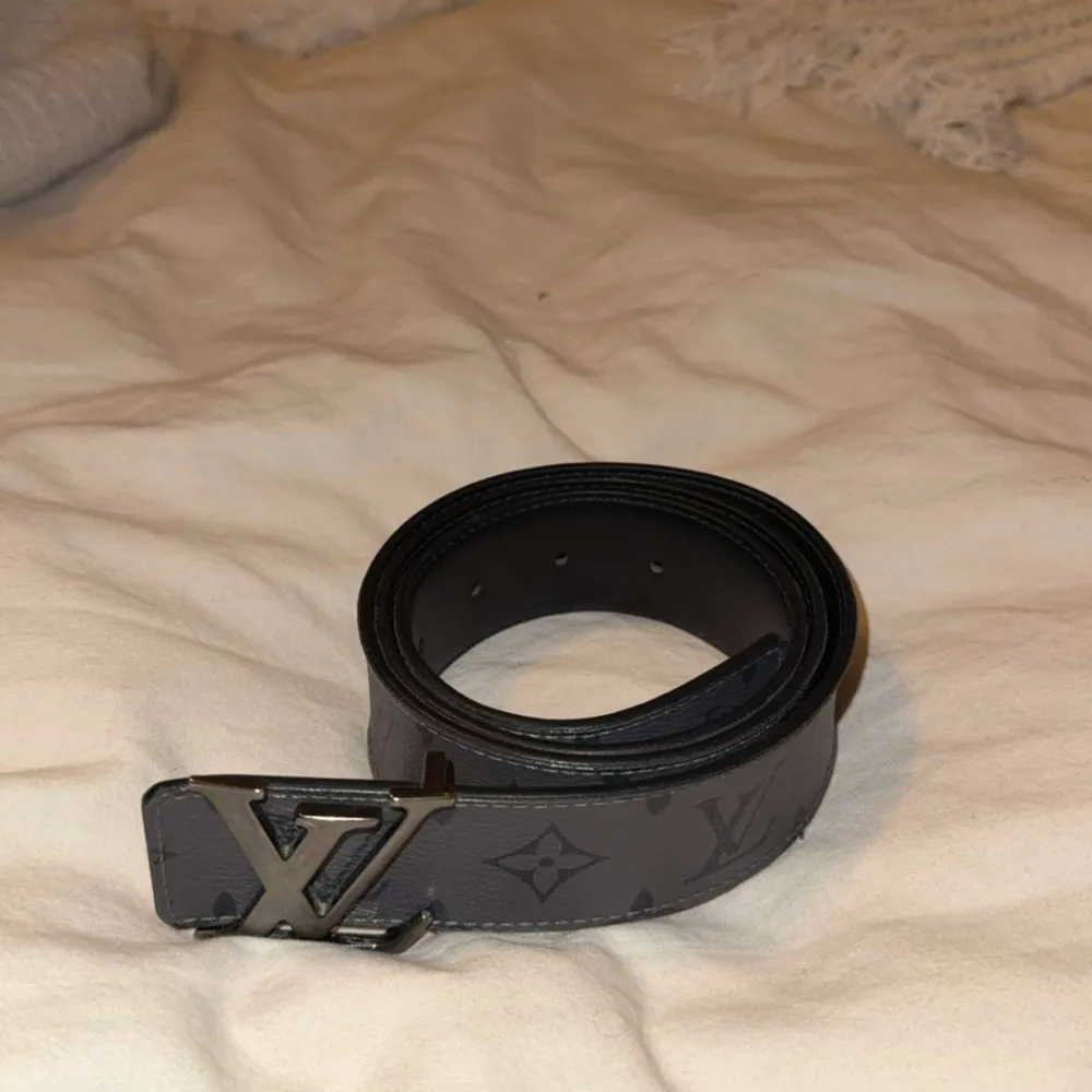 Snyggt grått bälte från Louis Vuitton med det klassiska LV-mönstret. Bältet har ett stilrent spänne i silverfärg med LV-logotypen. Perfekt för att ge din outfit en lyxig touch. . Muu.