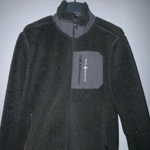 Svart fleecejacka från Sail Racing - Säljer en svart fleecejacka från Sail Racing med dragkedja och hög krage. Jackan har en praktisk bröstficka med dragkedja och logotyp. Perfekt för kyliga dagar. Passar folk som är mellan 158-163. Diskutera gärna pris med mig 