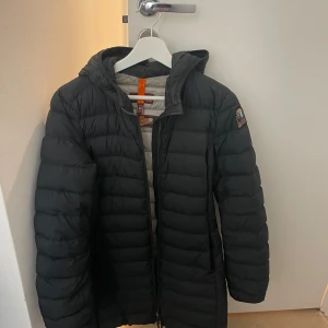 Svart dunjacka från Parajumpers - Säljer en svart dunjacka från Parajumpers med huva och dragkedja. Jackan har en quiltad design och är perfekt för kyligare väder. Den har en snygg logga på ärmen och är i storlek M.