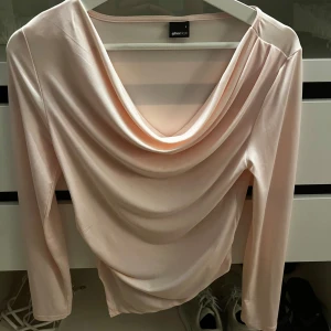 Ljusrosa topp från Gina Tricot - Säljer en elegant ljusrosa topp från Gina Tricot med draperad framsida och långa ärmar. Perfekt för en stilren look.