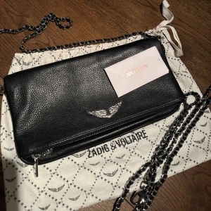 Svart axelväska från Zadig & Voltaire - Snygg svart axelväska i skinn från Zadig & Voltaire med kedjerem och ett coolt emblem framtill. En lång och en kort dragkedja. Dustvag och original kvitto ingår. Använt typ 2 gånger bara. 😆😆 