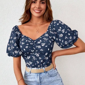 Blommig blus i blått - Charmig blommig blus i blått med vita blommor. Blusen har puffiga kortärmar och en smickrande v-ringning. Perfekt för en somrig look.