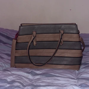 Brun och svart randig axelväska - Snygg brun och svart randig axelväska med dragkedja och justerbar axelrem. Väskan har ett rymligt inre med flera fack och en praktisk ytterficka med dragkedja. Perfekt för att bära med sig alla nödvändigheter. Använd fåtal ggr. 💗