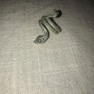 Silverfärgad ormring - Unik och stilren ring i form av en orm, silverfärgad med detaljerade mönster längs kroppen. Perfekt för att ge en edgy touch till din stil. Passar utmärkt för både vardag och speciella tillfällen.