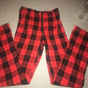 Röda rutiga byxor med dragkedja - Snygga röda byxor med svart rutmönster och dragkedja framtill. Perfekta för en trendig look med en skön passform. Passar utmärkt för höst och vinter.