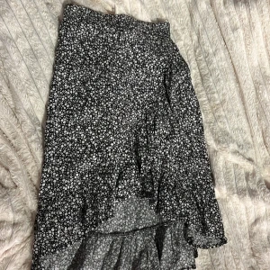 Svart blommig kjol med volang - Säljer en svart kjol med små vita blommor och volangdetaljer. Kjolen har en elastisk midja för bekväm passform. Jag har använt denna kjol ganska mycket, men säljer den då den inte är min stil💕
