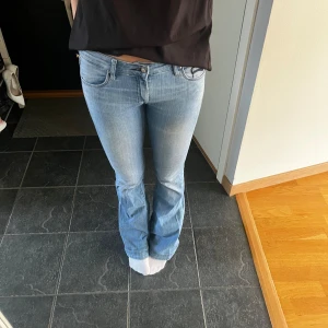 Ljusblå bootcut jeans - Säljer ett par snygga ljusblå bootcut jeans. De är lågmidjade och har en klassisk femficksdesign med snygga detaljer vid fickorna. Perfekta för en avslappnad vardagslook! Utsvängda. Innerbenslängden är 82 och midjemått 37,5 