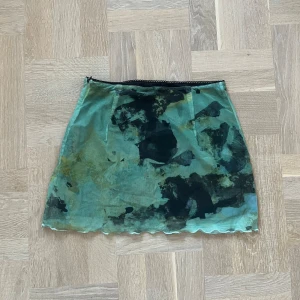 Grön mönstrad kjol - Säljer en supercool grön kjol med ett abstrakt mönster. Kjolen har en kort längd och är perfekt för både vardag och fest. Den har en elastisk midja för en bekväm passform. Materialet känns lätt och luftigt, vilket gör den idealisk för varmare dagar.