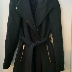Svart, grå kappa med bälte - Säljer en mörk grå kappa med bälte i midjan. Den har långa ärmar och två dragkedjefickor. Den är för höst och vinter. Använt den en månad! Den har en liten skada där bak, men lätt att fixa hos en skräddare. Köpt från Vero Moda! Pris kan diskuteras! 😍