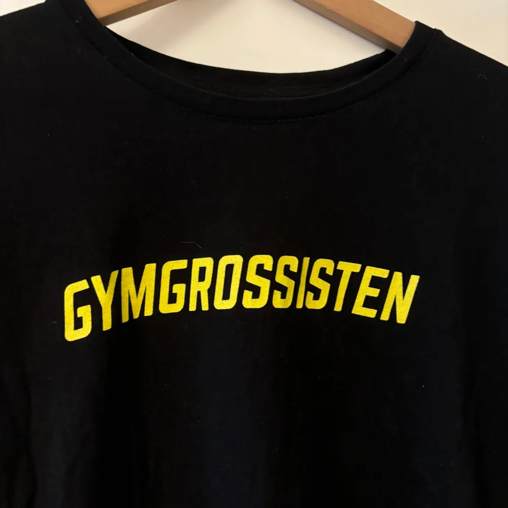 Säljer en svart t-shirt från Gymgrossisten i storlek XL. Den har en enkel design med texten 'GYMGROSSISTEN' i gult på framsidan. Perfekt för träning eller vardagsbruk! T-shirten är i nyskick!. T-shirts.