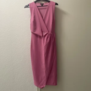 Rosa klänning från Boohoo - Säljer en snygg rosa klänning från Boohoo i storlek M. Klänningen är ärmlös med en omlott-design framtill och en v-ringad hals. Perfekt för festliga tillfällen!