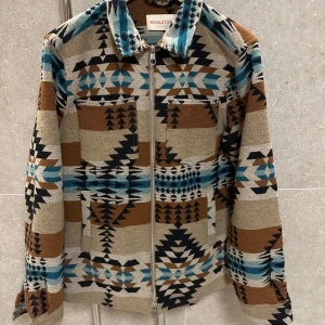 Mönstrad jacka med dragkedja - Säljer en snygg mönstrad jacka från revolution med dragkedja. Jackan har ett unikt geometriskt mönster som ger ett väldigt western stuk. Perfekt för att sticka ut i mängden! 