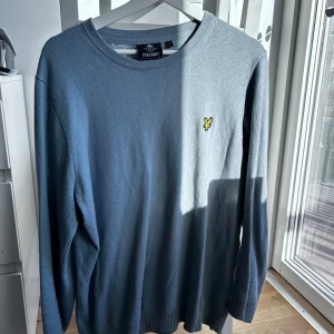 Ljusblå tröja från Lyle & Scott - Säljer en stilren ljusblå tröja från Lyle & Scott i storleken L med deras ikoniska gula logga på bröstet. Tröjan har långa ärmar och en rund halsringning, perfekt för en avslappnad look. Hör av er vid intresse/ frågor!