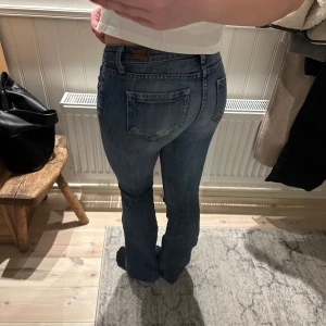 Blå jeans med bootcut - Säljer ett par klassiska blå jeans med bootcut. De har en snygg tvätt och är perfekta för en avslappnad stil. Jeansen har en låg midja och är tillverkade i denim. Finns hål i skrevet och har tidigare lagat dem där så det är bara att göra det igen har bara inte haft tiden själv! Syns annars inte om du väljer att inte sy dem!