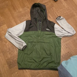 Grön och svart vindjacka från The North Face, den är lite för stor på mig men passar endå bra (jag är 176cm) - Säljer en grön och svart vindjacka från The North Face med huva och dragkedja. Jackan har en stor ficka framtill och är perfekt för blåsiga dagar. Den har långa ärmar i en kontrasterande ljusgrå färg.