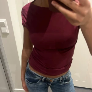 Vinröd topp - Säljer en vinröd topp med korta ärmar och rund halsringning. Toppen har en tight passform och är perfekt för en stilren look. Passar bra till jeans eller kjol.