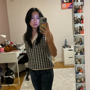 Svartvit rutig väst - Snygg svartvit rutig väst med v-ringad design. Perfekt för att lägga till en stilren touch till din outfit. Passar bra till jeans eller kjol.
