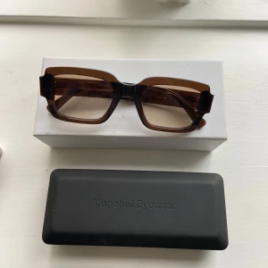 Bruna fyrkantiga solglasögon från Monokel Eyewear - Snygga bruna solglasögon med fyrkantig form från Monokel Eyewear. De har en stilren design med breda skalmar och en transparent brun nyans. Modellen heter apollo och färgen heter cola. Liten reva ( syns inte när de är på), annars inga anmärkningar. Originalfärpackning hänger med :) 