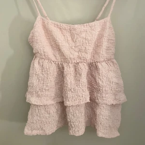 Ljusrosa volangtopp - Söt ljusrosa topp med volanger och smala axelband. Perfekt för varma sommardagar med sin luftiga design och mjuka textur.💕🌸 säljer då den aldrig kommer till användning, perfekt skick och sann i storlek🌟