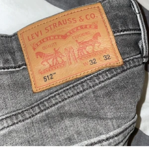 Grå Levis 512 jeans - Snygga grå Levis 512 jeans med en klassisk straight passform. De har en midwaist design och är perfekta för en avslappnad stil. Jeansen har de ikoniska bakfickorna med Levis logga och en dragkedja framtill.